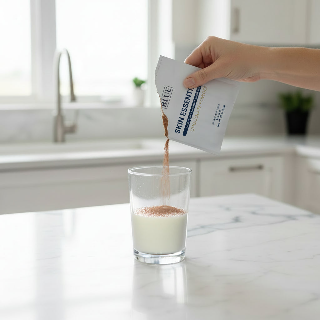 Person pouring a powder from a package labeled 'Blue' into a glass of milk on a kitchen counter.